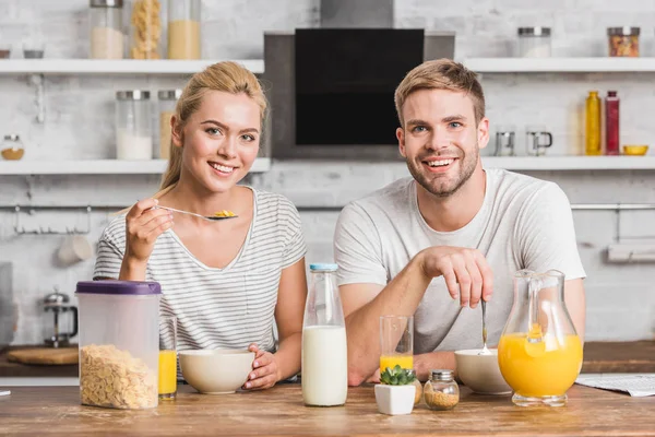 Lächelndes Paar blickt in die Kamera und frühstückt in der Küche — Stockfoto