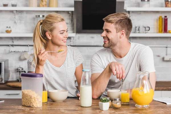 Sonriente pareja desayunando y mirándose en la cocina - foto de stock