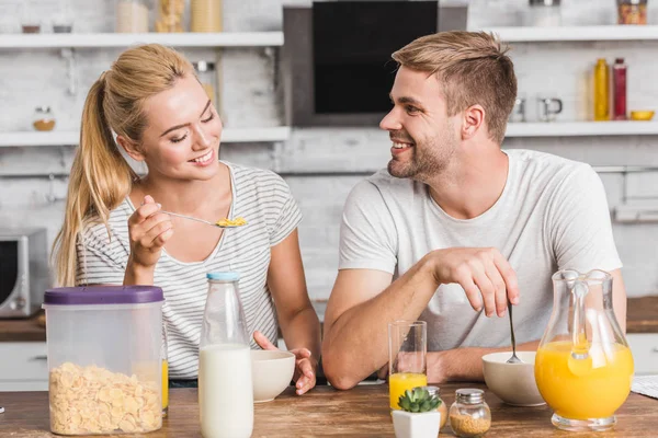 Couple souriant manger des flocons de maïs avec du lait sur le petit déjeuner dans la cuisine — Photo de stock