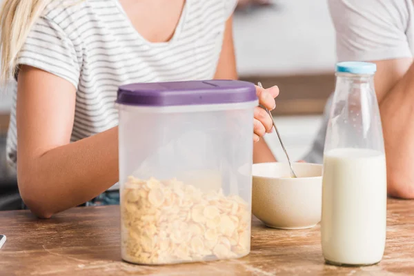 Image recadrée de couple prenant le petit déjeuner dans la cuisine, flocons de maïs et bouteille de lait sur la table — Photo de stock