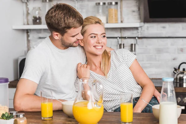 Парень обнимает улыбающуюся девушку во время завтрака на кухне — стоковое фото