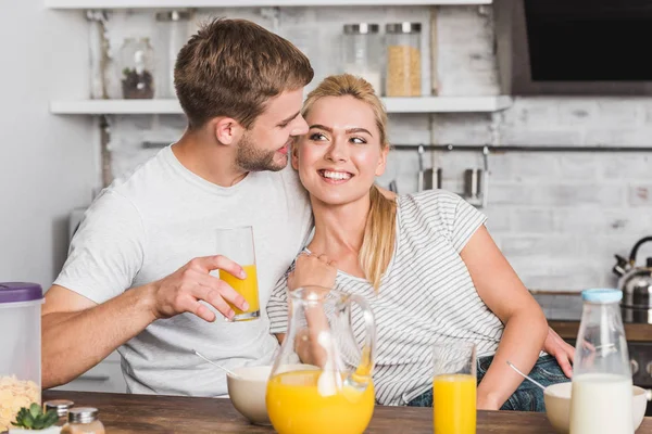 Novio feliz abrazando novia durante el desayuno en la cocina y se miran el uno al otro - foto de stock