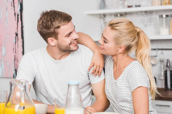 Pareja feliz mirándose en la mesa en la cocina - foto de stock