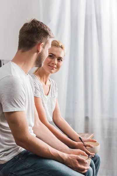 Pareja sosteniendo platos con el desayuno y mirándose en la cocina - foto de stock