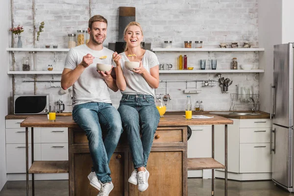 Feliz pareja desayunando y sentado en el mostrador de la cocina - foto de stock