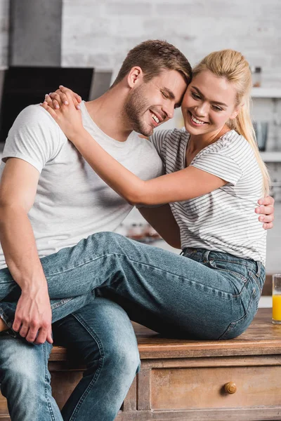 Casal feliz abraçando e sentado no balcão da cozinha — Fotografia de Stock