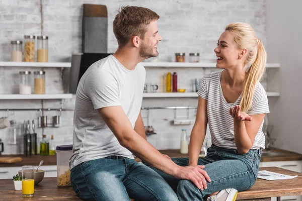 Glückliches Paar im Gespräch und auf dem Küchentisch sitzend — Stockfoto