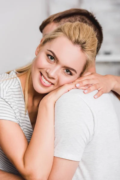 Retrato de novia sonriente abrazando novio y mirando a la cámara en casa - foto de stock