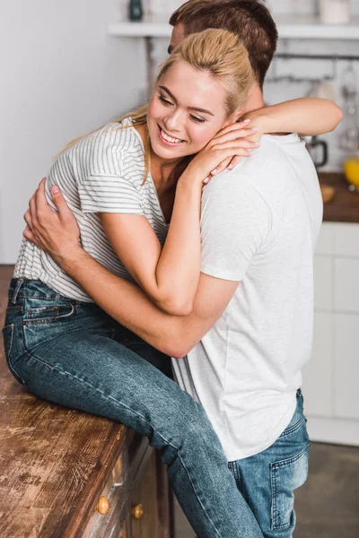 Novia feliz sentado en el mostrador de la cocina y abrazando novio - foto de stock