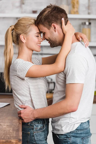 Vista lateral de la feliz pareja abrazándose en la cocina - foto de stock
