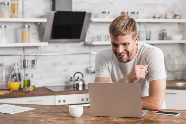 Sourire beau freelance regardant ordinateur portable dans la cuisine — Photo de stock