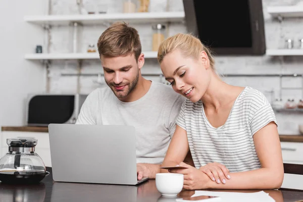 Sorrindo jovem casal com cartão de crédito usando laptop em casa — Fotografia de Stock