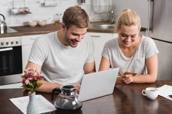 Vue grand angle de sourire jeune couple avec carte de crédit à l'aide d'un ordinateur portable à la maison — Photo de stock