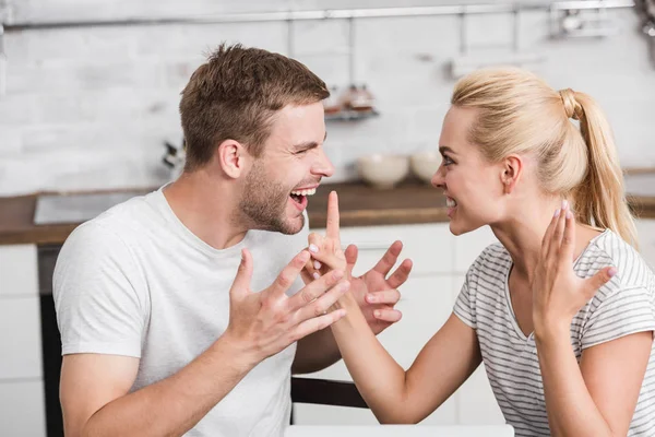 Side view of emotional young couple arguing and looking at each other in kitchen — Stock Photo