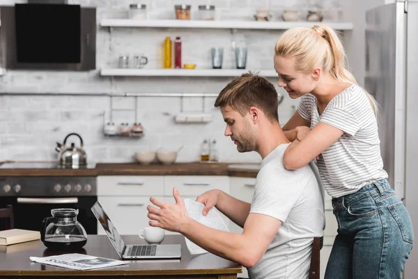 Vista laterale della giovane coppia che utilizza il computer portatile insieme a casa — Foto stock