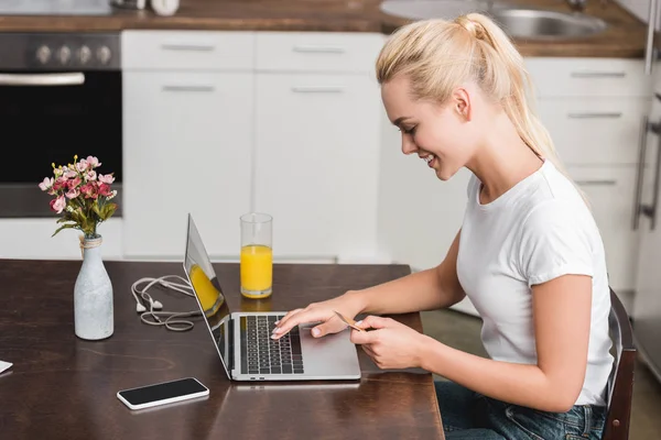 Вид збоку усміхненої молодої жінки, що тримає кредитну картку і використовує ноутбук вдома — стокове фото