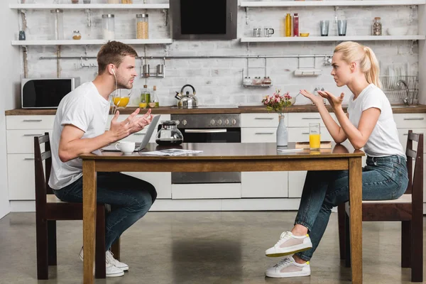 Vue latérale de jeunes couples émotionnels se disputant pendant le petit déjeuner dans la cuisine — Photo de stock