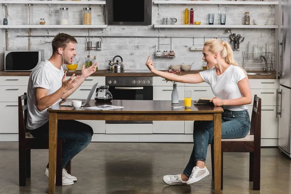 Vue latérale de jeunes couples se disputant pendant le petit déjeuner dans la cuisine — Photo de stock