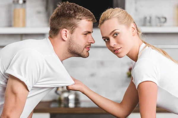 Attractive young woman holding t-shirt of handsome boyfriend and looking at camera — Stock Photo