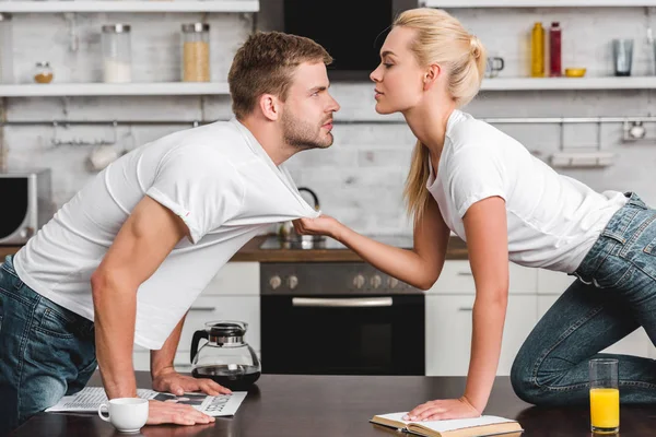 Vista lateral do jovem casal olhando um para o outro, jovem mulher segurando t-shirt de namorado bonito na cozinha — Fotografia de Stock