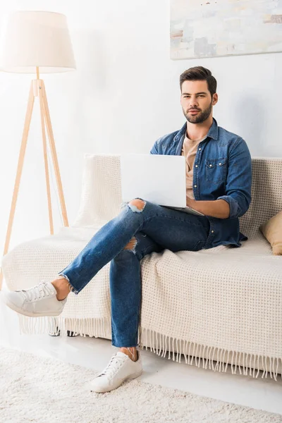 Усміхнений чоловічий фрілансер, що працює з ноутбуком на дивані вдома — стокове фото