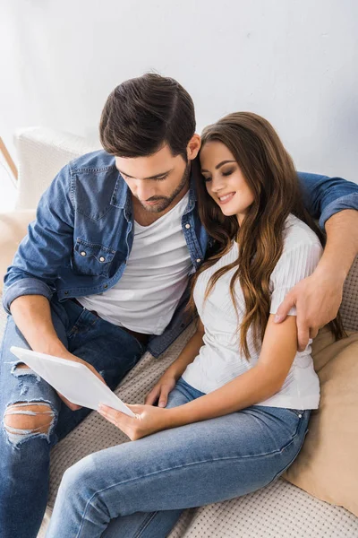 Vue grand angle de jeune couple assis sur le canapé avec tablette numérique à la maison — Photo de stock