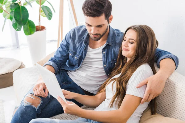 Молода пара сидить на дивані з цифровим планшетом вдома — стокове фото