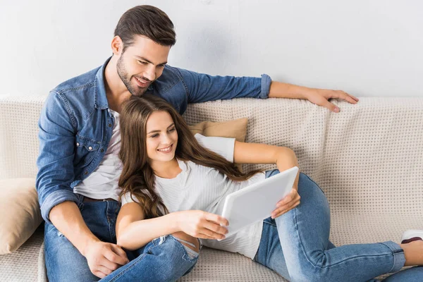 Feliz joven pareja viendo tableta digital en el sofá en casa - foto de stock