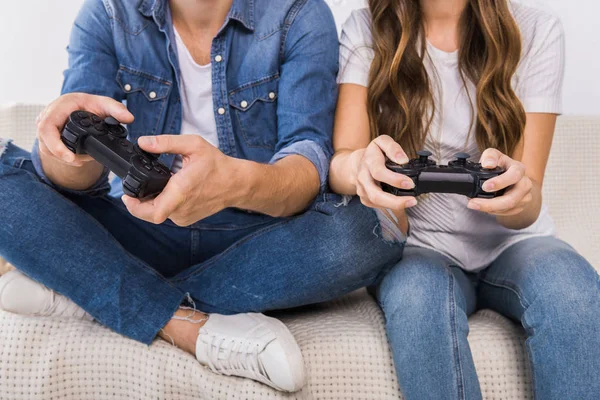 Imagen recortada de pareja jugando videojuego por joysticks en el sofá en casa - foto de stock