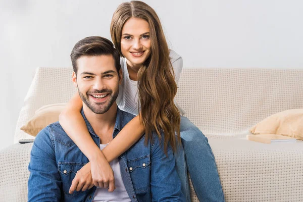 Portrait of young smiling couple looking at camera on sofa at home — Stock Photo