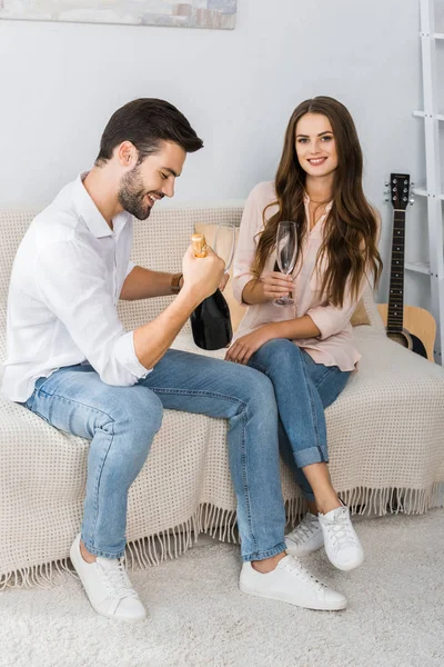 Happy young couple celebrating with bottle of champagne and glasses on couch at home — Stock Photo