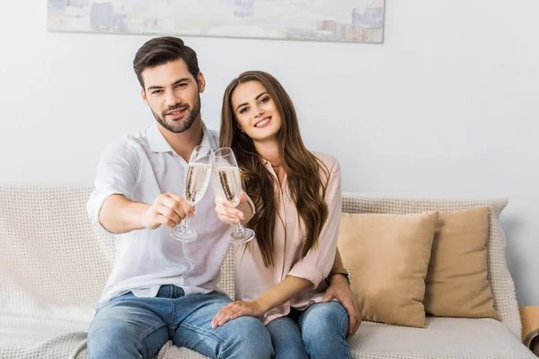 Jeune couple cliquetis verres de champagne sur le canapé à la nouvelle maison — Photo de stock