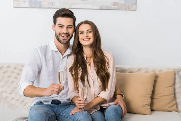 Portrait of happy young couple with glasses of champagne resting on sofa at home — Stock Photo