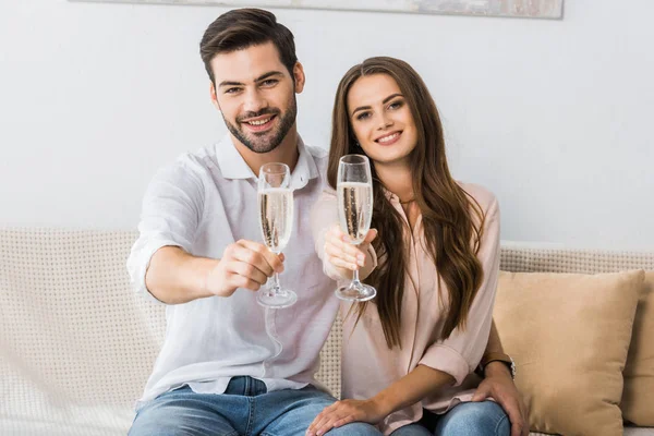 Portrait de heureux jeune couple avec des verres de champagne reposant sur le canapé à la maison — Photo de stock