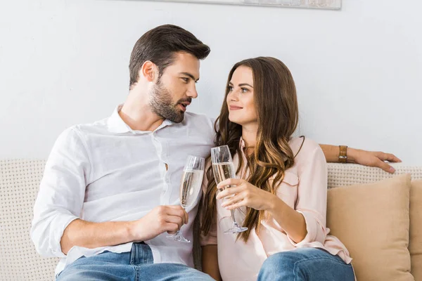 Retrato de pareja tintineo copas de champán en el sofá en el nuevo hogar - foto de stock