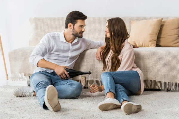 Man pouring champagne into glass while sitting on floor together with girlfriend at home — Stock Photo