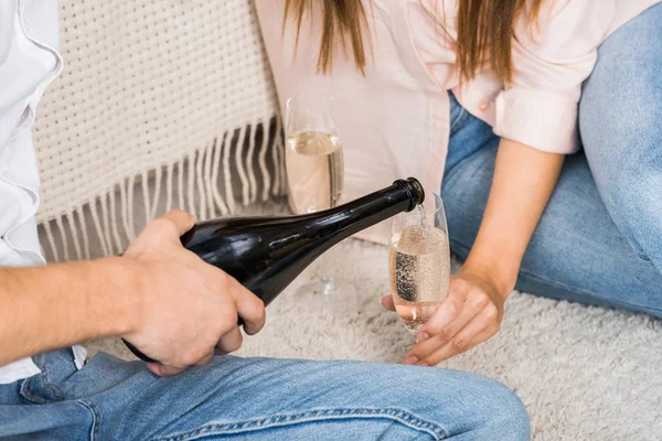 Teilbild eines Mannes, der Champagner ins Glas gießt, während er mit Freundin zu Hause auf dem Boden sitzt — Stockfoto