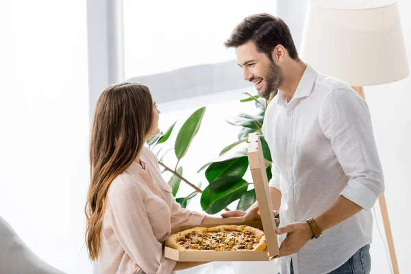 Vista laterale della giovane coppia con pizza delirante in scatola di carta a casa — Foto stock