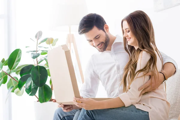 Усміхнена пара з піцою в паперовій коробці сидить на дивані вдома — стокове фото