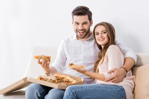 Portrait de jeune couple souriant avec pizza sur canapé à la maison — Photo de stock
