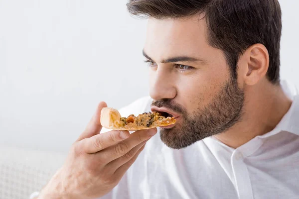 Retrato de un joven comiendo pizza solo en casa - foto de stock