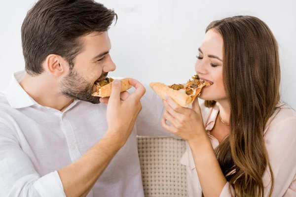 Retrato de pareja joven comiendo pizza en el sofá en casa - foto de stock