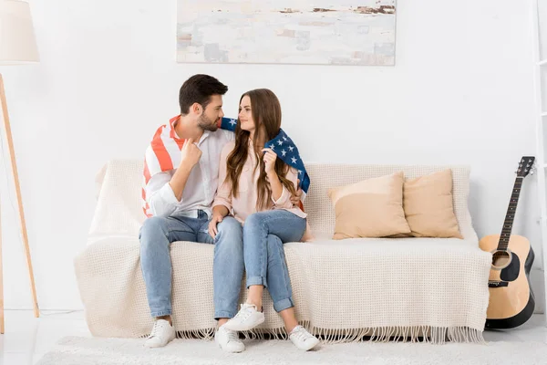 Young couple covered with american flag resting on sofa at home — Stock Photo