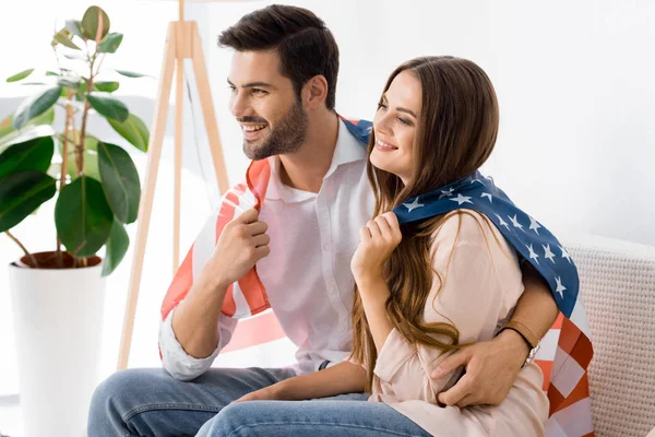 Young couple covered with american flag resting on sofa at home — Stock Photo