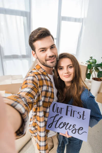 Punto de vista de la cámara de la pareja sonriente con nuestra primera tarjeta de la casa tomando selfie juntos en el nuevo hogar - foto de stock