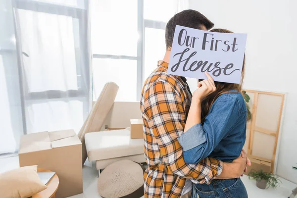 Oscurecido vista de pareja besándose detrás de nuestra primera tarjeta de casa en nuevo hogar - foto de stock