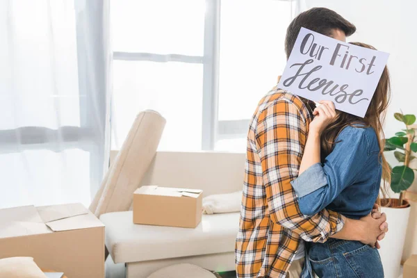 Obscured view of couple kissing behind our first house card at new home — Stock Photo