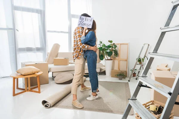 Visão obscurecida de casal beijando atrás de nosso primeiro cartão de casa em nova casa — Fotografia de Stock