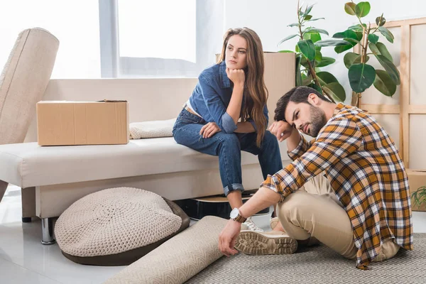 Pensive young couple at new house with cardboard boxes, moving home concept — Stock Photo