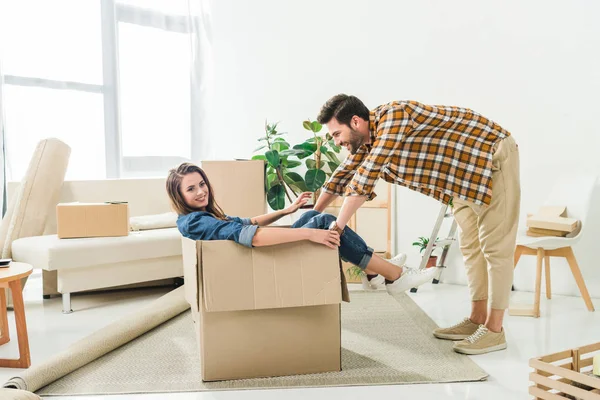 Vista lateral do casal se divertindo com caixa de papelão na nova casa, movendo-se para casa conceito — Fotografia de Stock